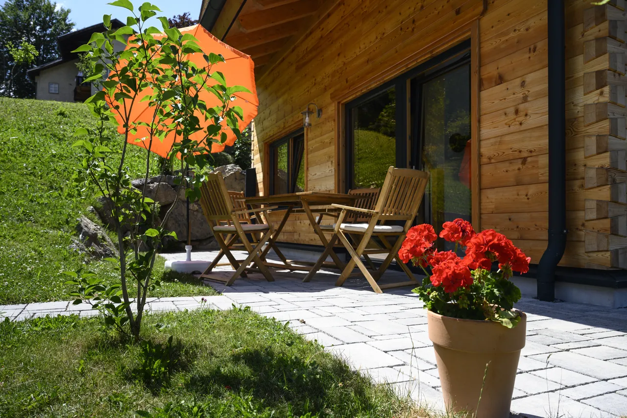 Sonnenterrasse mit Holzstühlen, Sonnenschirm und Geranien