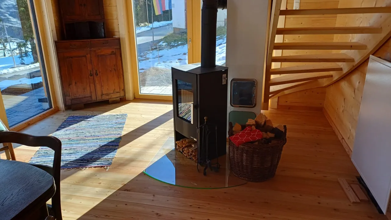 Kaminofen im Wohnraum, durch die großen Fenster sieht man den Schnee draußen