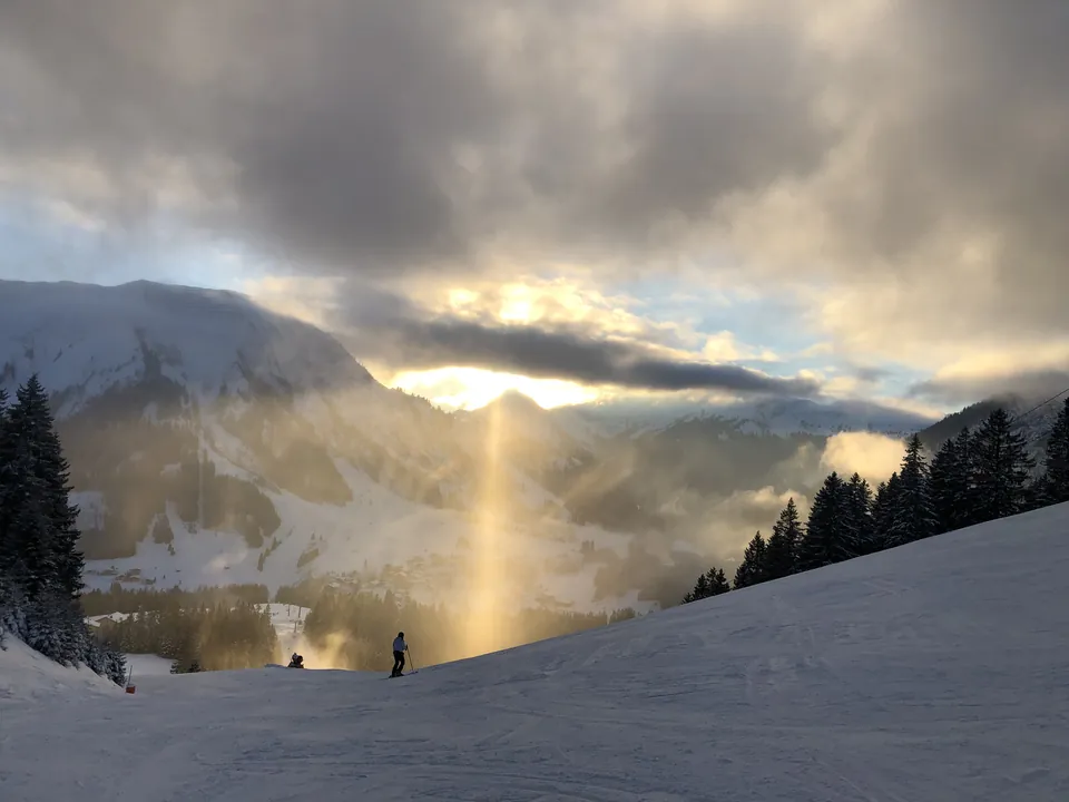 Skipiste oberhalb von Berwang im Gegenlicht, Wolken und Sonnenstrahlen über dem verschneiten Tal