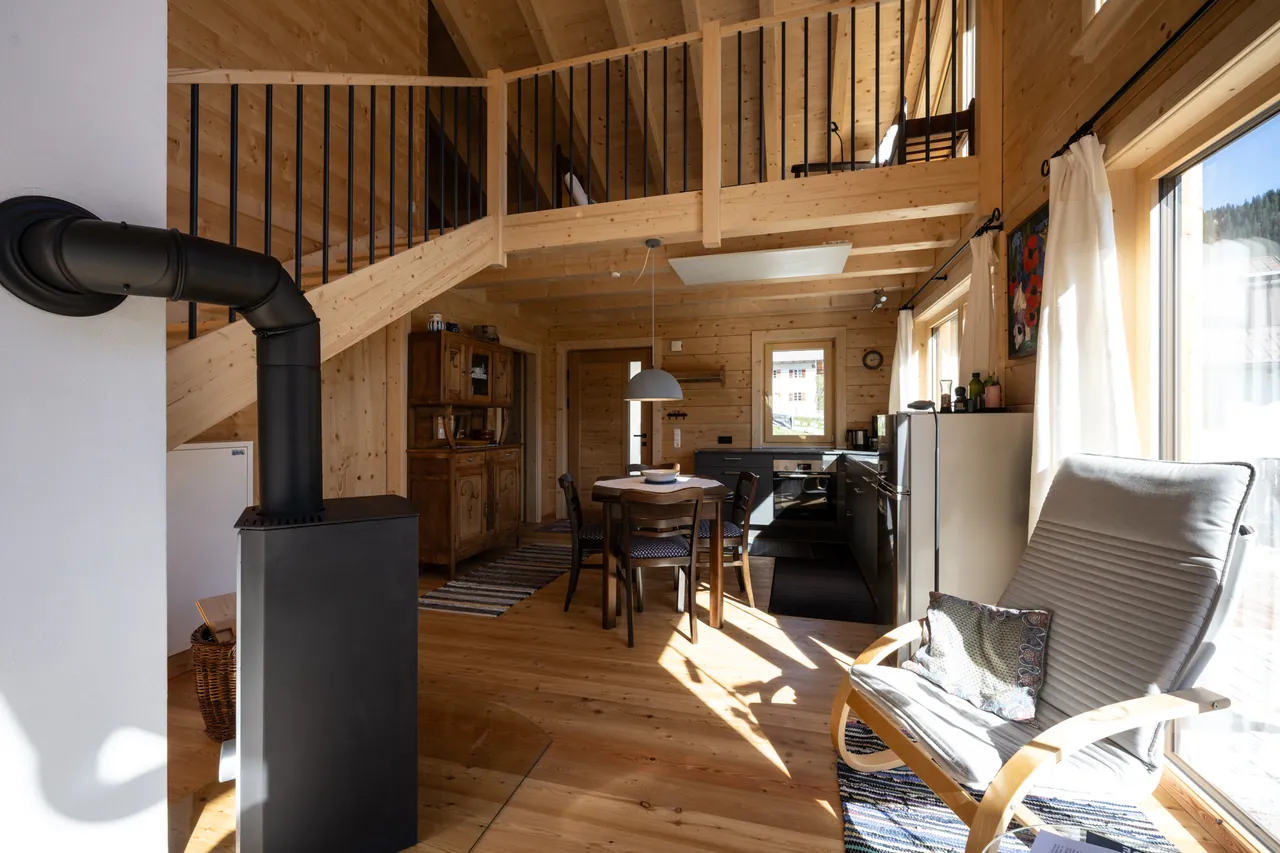 Lichtdurchfluteter Wohnraum mit Kaminofen, Holzdecke und Blick hinauf zur Galerie